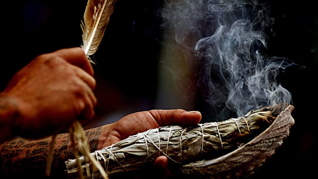 A person holding a feather and smoke in their hands.